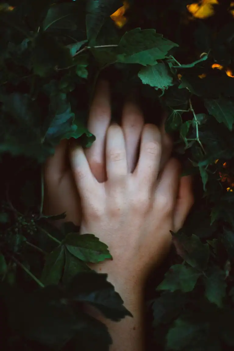 Hands intertwined among green leaves.